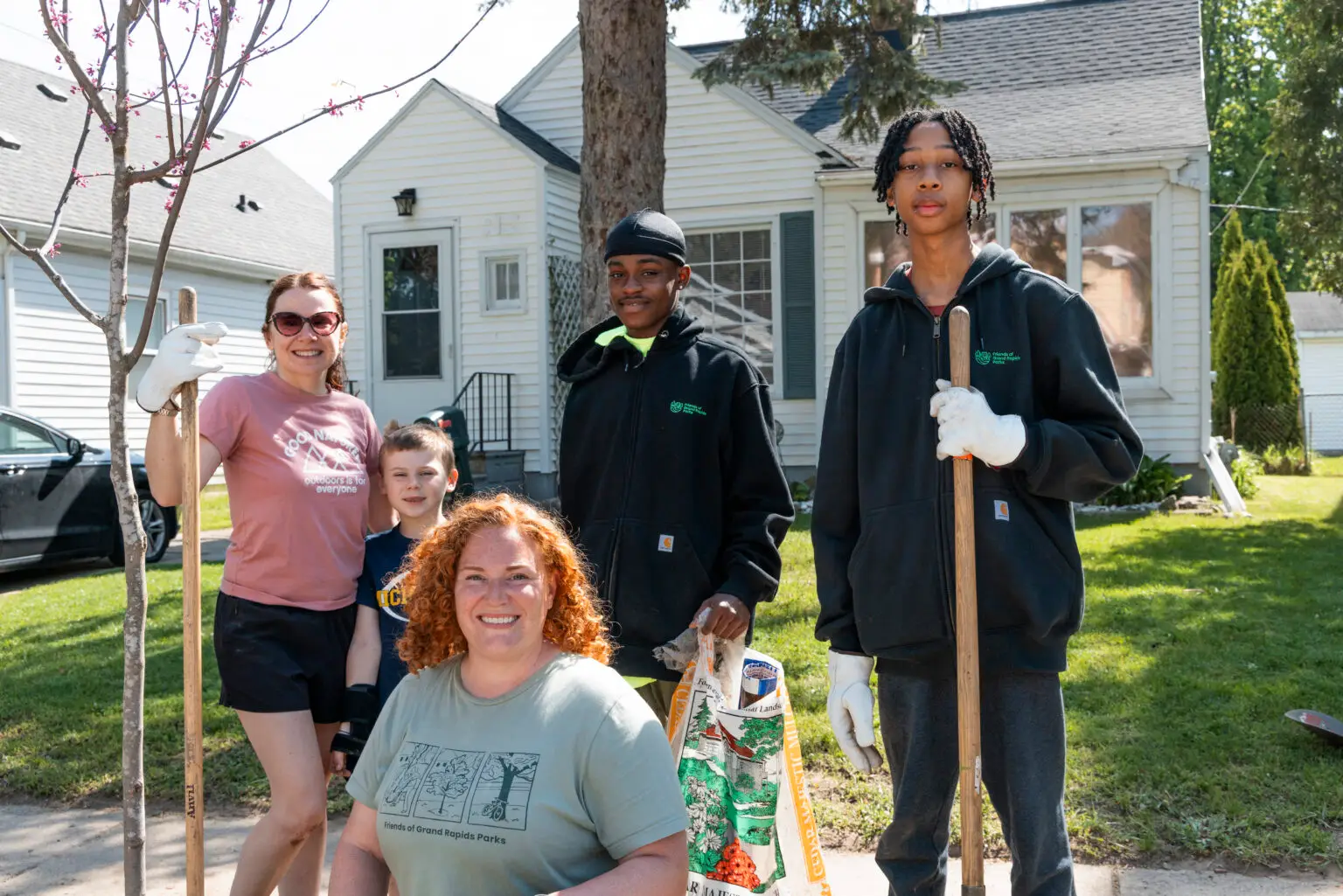 Adults and youth smile together with gardening tools, working side by side for a greener, healthier community.