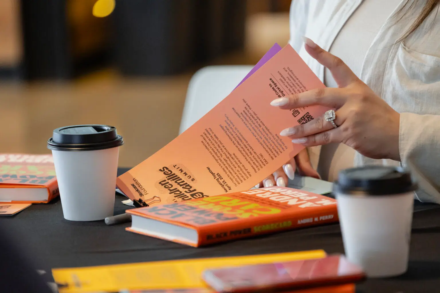 Hands turning a book’s pages at a table with study materials and coffee, evoking learning and shared opportunity.