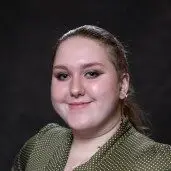Young woman in a green polka dot blouse smiles warmly, reflecting openness and inclusion on a dark background.