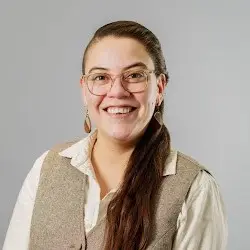 Friendly woman with glasses and a warm smile, dressed in business-casual attire, suggests a welcoming community spirit.