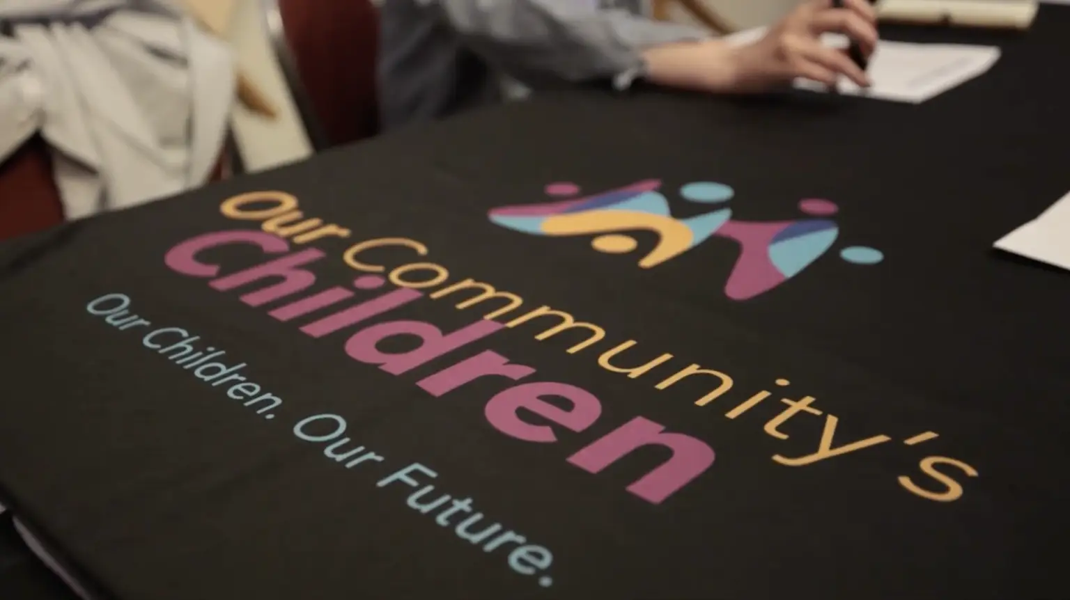 A black-clothed table with a bright Our Community’s Children logo, symbolizing unity and opportunity in education.